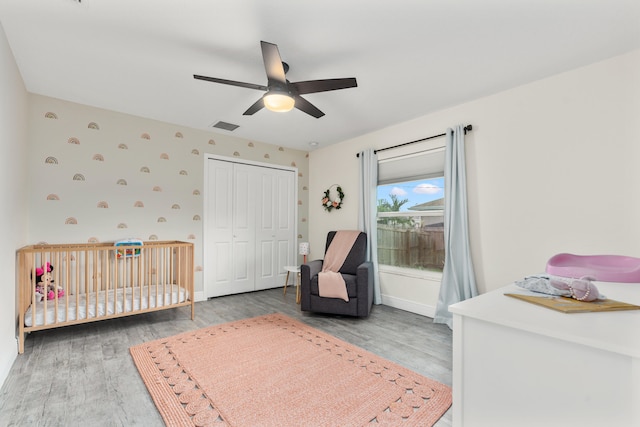 bedroom with ceiling fan, hardwood / wood-style flooring, a crib, and a closet