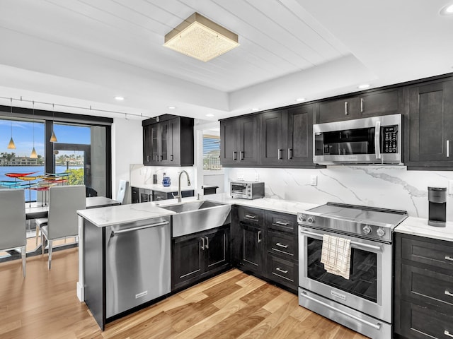 kitchen with light stone countertops, tasteful backsplash, stainless steel appliances, sink, and light hardwood / wood-style flooring