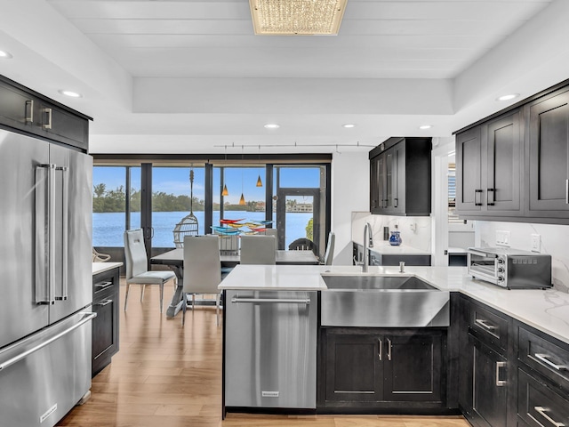 kitchen with sink, light hardwood / wood-style floors, decorative backsplash, a water view, and appliances with stainless steel finishes