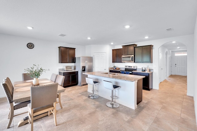 kitchen with an island with sink, sink, dark brown cabinets, appliances with stainless steel finishes, and a breakfast bar area