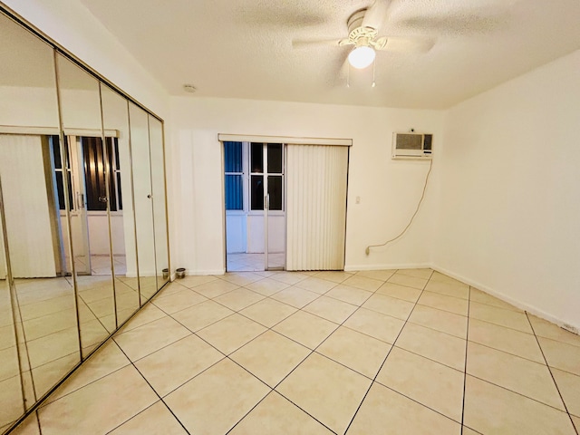 unfurnished bedroom featuring a wall mounted air conditioner, a textured ceiling, ceiling fan, light tile patterned floors, and a closet