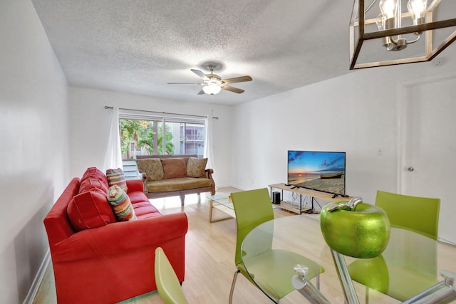 living room with light hardwood / wood-style flooring, a textured ceiling, and ceiling fan with notable chandelier