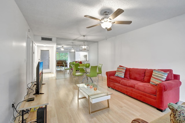 living room featuring light hardwood / wood-style flooring, a textured ceiling, and ceiling fan