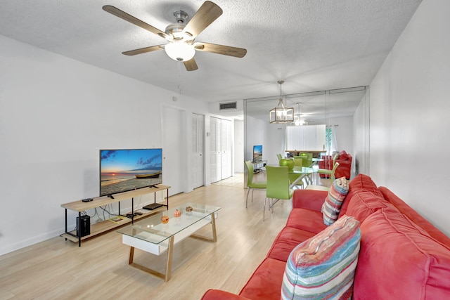 living room with light hardwood / wood-style floors, a textured ceiling, and ceiling fan with notable chandelier