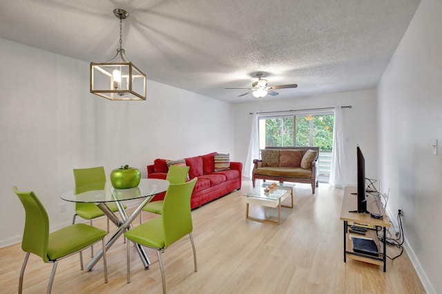 living room with a textured ceiling, light wood-type flooring, and ceiling fan with notable chandelier