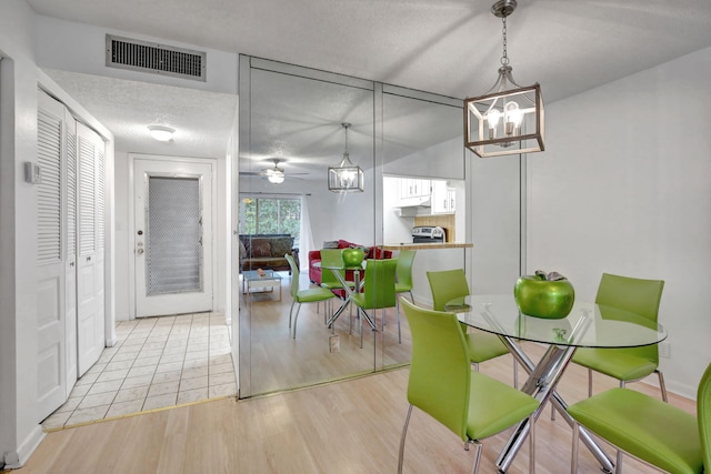 dining room with a textured ceiling, ceiling fan with notable chandelier, and light wood-type flooring