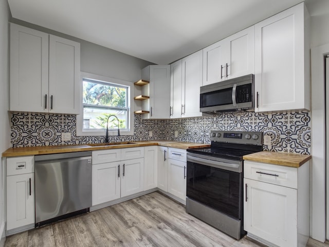 kitchen with tasteful backsplash, butcher block counters, light wood-style flooring, stainless steel appliances, and a sink