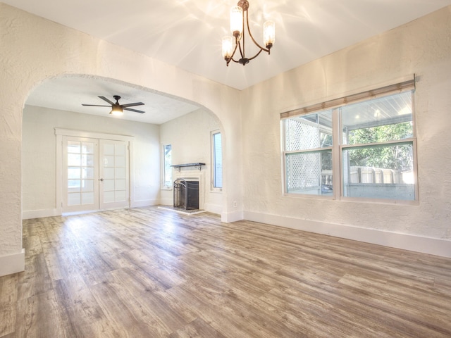 unfurnished living room featuring hardwood / wood-style floors, ceiling fan with notable chandelier, and french doors