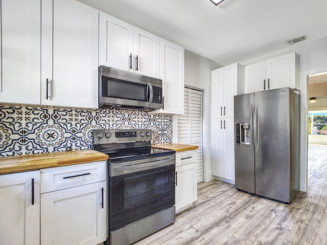 kitchen with stainless steel appliances, tasteful backsplash, butcher block countertops, white cabinets, and light wood-type flooring