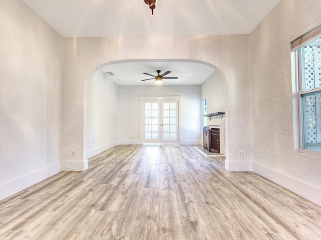 unfurnished living room with arched walkways, a fireplace with raised hearth, a textured wall, wood finished floors, and baseboards