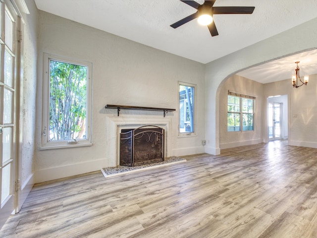 unfurnished living room with a fireplace with raised hearth, arched walkways, a textured ceiling, wood finished floors, and baseboards