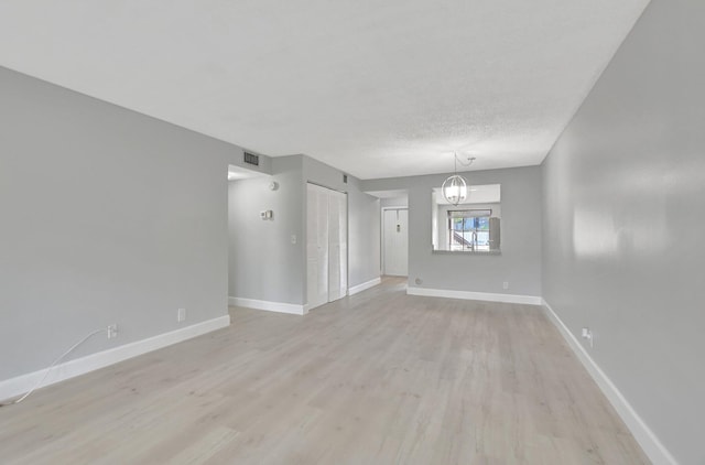 spare room with a textured ceiling, light hardwood / wood-style floors, and an inviting chandelier