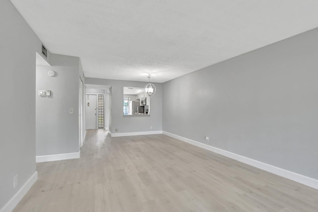 empty room featuring an inviting chandelier, light hardwood / wood-style floors, and a textured ceiling