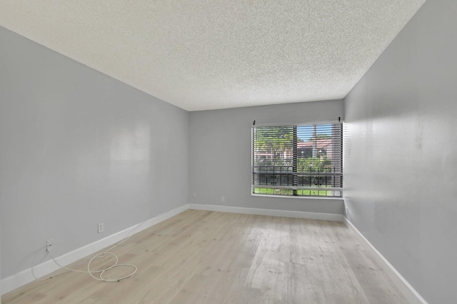 empty room with a textured ceiling and light hardwood / wood-style flooring