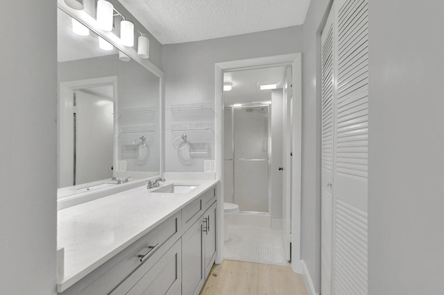 bathroom featuring wood-type flooring, a textured ceiling, an enclosed shower, vanity, and toilet