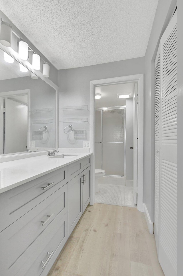 bathroom with a textured ceiling, walk in shower, hardwood / wood-style floors, vanity, and toilet