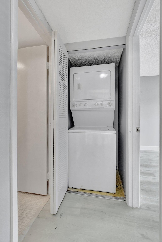 clothes washing area with stacked washer / drying machine, a textured ceiling, and light wood-type flooring