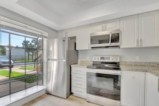 kitchen featuring a tray ceiling, light hardwood / wood-style floors, white cabinets, appliances with stainless steel finishes, and light stone countertops