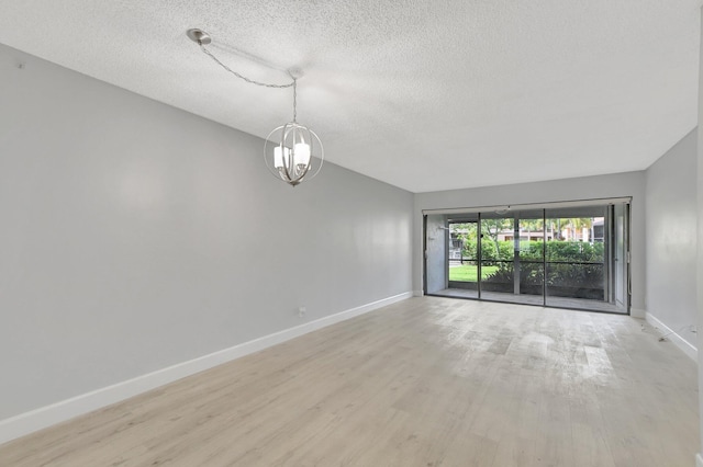 empty room featuring an inviting chandelier, a textured ceiling, and light hardwood / wood-style flooring