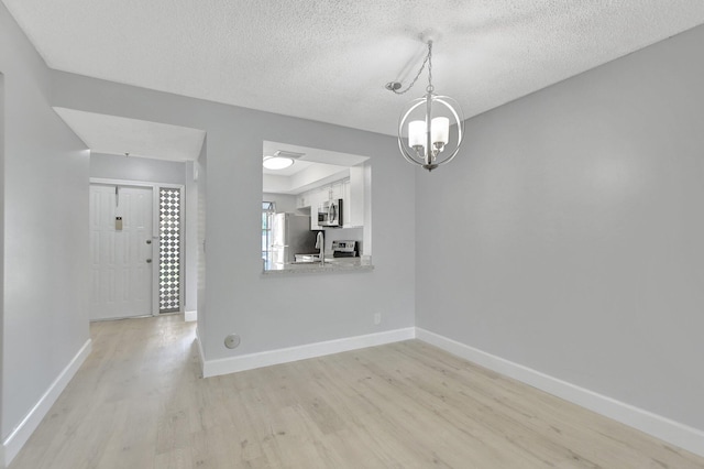 unfurnished dining area featuring a textured ceiling, a chandelier, light hardwood / wood-style floors, and sink