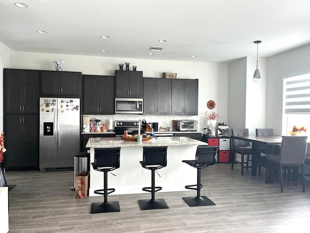 kitchen with a breakfast bar area, pendant lighting, stainless steel appliances, and light stone counters