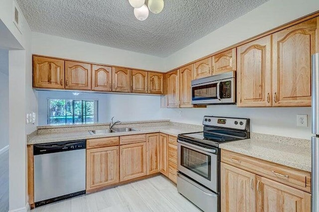 kitchen featuring light wood-type flooring, a textured ceiling, sink, stainless steel appliances, and light brown cabinets