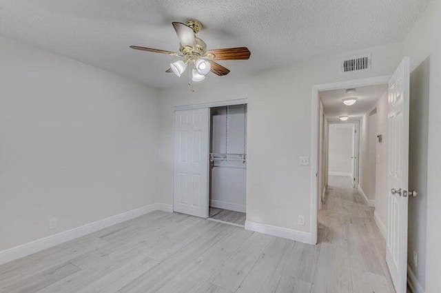 unfurnished bedroom featuring light hardwood / wood-style flooring, a closet, ceiling fan, and a textured ceiling