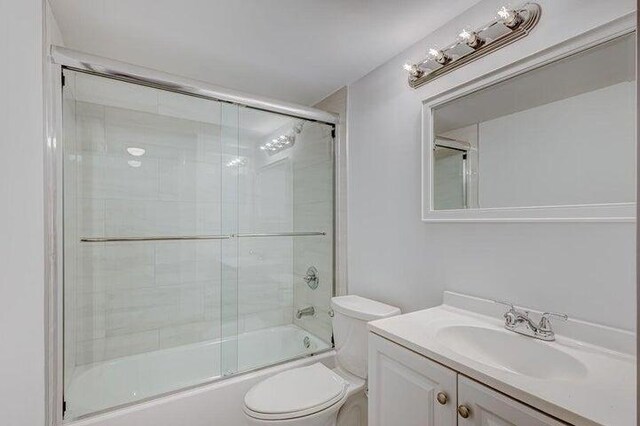 full bathroom with enclosed tub / shower combo, vanity, and toilet