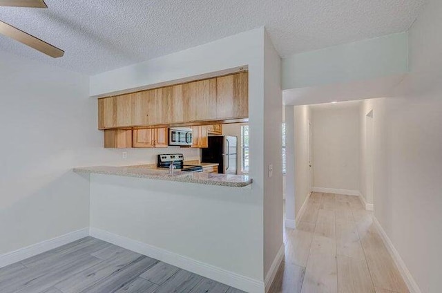 kitchen with kitchen peninsula, a textured ceiling, stainless steel appliances, light brown cabinetry, and light wood-type flooring