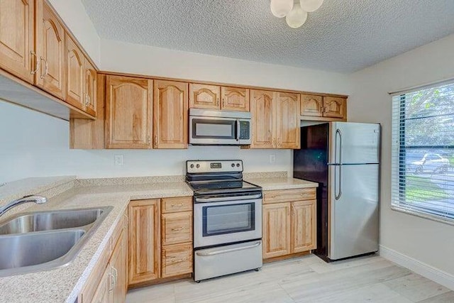 kitchen featuring stainless steel appliances, a textured ceiling, light brown cabinets, and sink