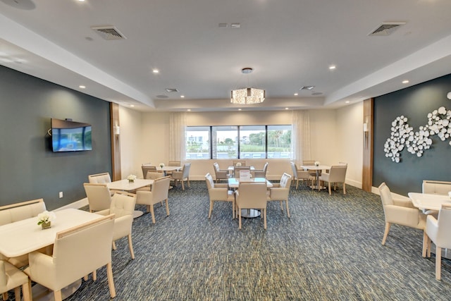 dining room featuring dark carpet, an inviting chandelier, and a tray ceiling