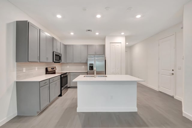 kitchen featuring tasteful backsplash, gray cabinetry, stainless steel appliances, light hardwood / wood-style flooring, and a center island with sink