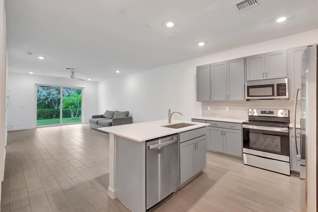 kitchen with sink, gray cabinetry, backsplash, a center island with sink, and appliances with stainless steel finishes