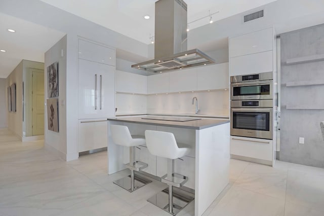 kitchen with white cabinets, island exhaust hood, a center island, double oven, and a breakfast bar