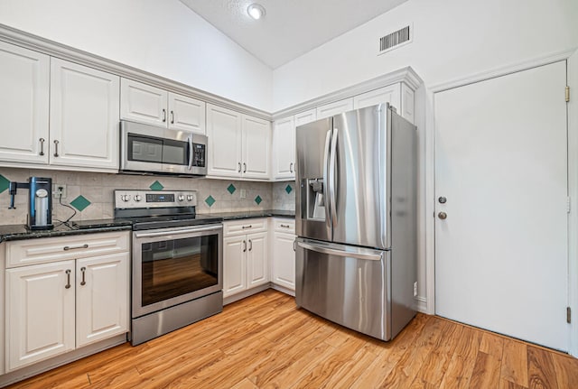 kitchen with light hardwood / wood-style flooring, dark stone counters, white cabinetry, appliances with stainless steel finishes, and tasteful backsplash