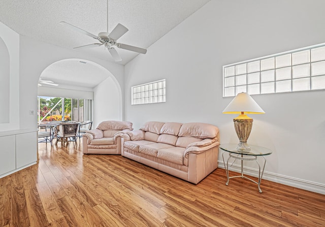 living room featuring light hardwood / wood-style flooring, a textured ceiling, high vaulted ceiling, and ceiling fan