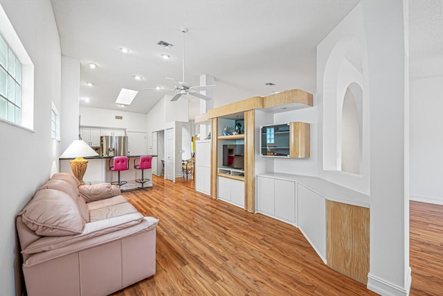 living room featuring a skylight, high vaulted ceiling, light wood-type flooring, and ceiling fan