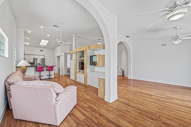 living room featuring vaulted ceiling, light hardwood / wood-style flooring, a textured ceiling, and ceiling fan