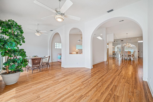 interior space with ceiling fan with notable chandelier and light wood-type flooring