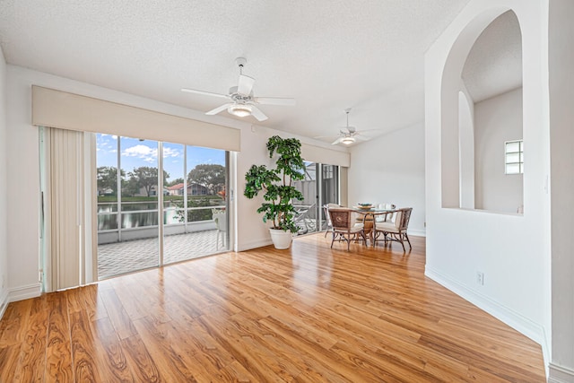 interior space with a textured ceiling, a water view, light wood-type flooring, and ceiling fan