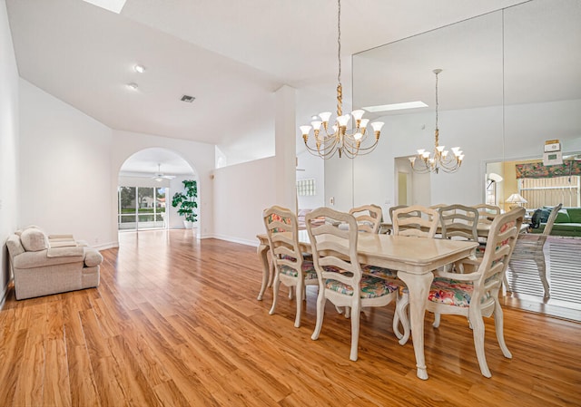 dining room with high vaulted ceiling, ceiling fan with notable chandelier, and light wood-type flooring