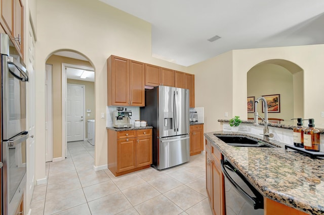 kitchen featuring sink, light tile patterned flooring, light stone counters, stainless steel appliances, and washer / dryer