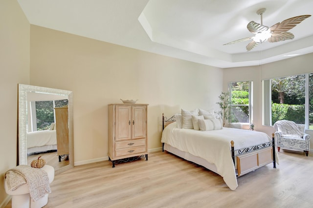 bedroom featuring ceiling fan, a raised ceiling, and light hardwood / wood-style flooring