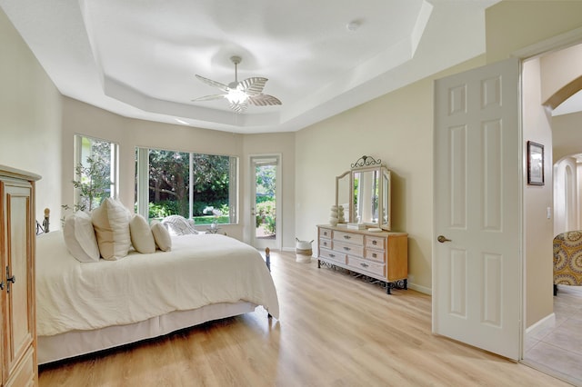 bedroom featuring light wood-type flooring, a tray ceiling, and ceiling fan