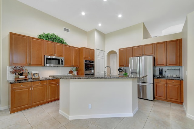 kitchen with backsplash, high vaulted ceiling, a kitchen island with sink, and appliances with stainless steel finishes