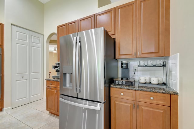 kitchen featuring stainless steel refrigerator with ice dispenser, backsplash, dark stone counters, light tile patterned floors, and oven