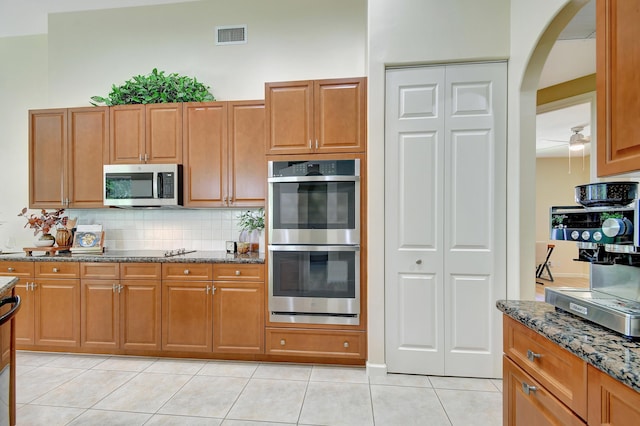 kitchen featuring appliances with stainless steel finishes, tasteful backsplash, light tile patterned floors, and dark stone counters