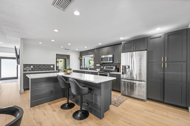 kitchen featuring stainless steel appliances, light wood-type flooring, a kitchen bar, and a center island