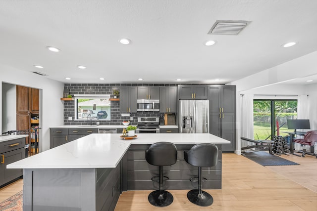 kitchen with gray cabinets, stainless steel appliances, light hardwood / wood-style floors, and a center island