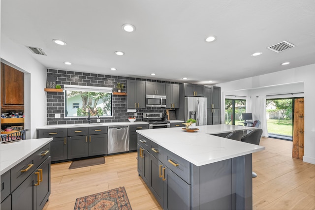 kitchen with gray cabinets, light wood-type flooring, a center island, backsplash, and appliances with stainless steel finishes